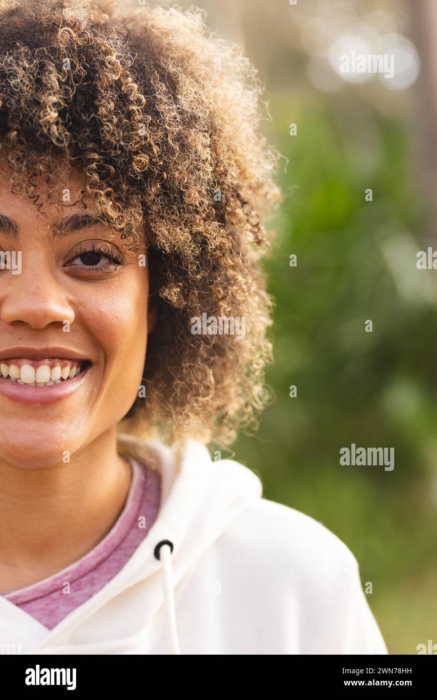 Young biracial woman smiles warmly on a hike, her curly hair framing her face Stock Photo