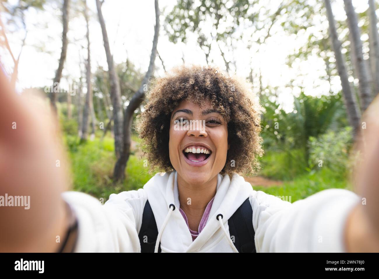 Young biracial woman with curly hair takes a selfie in a forested area on a hike Stock Photo