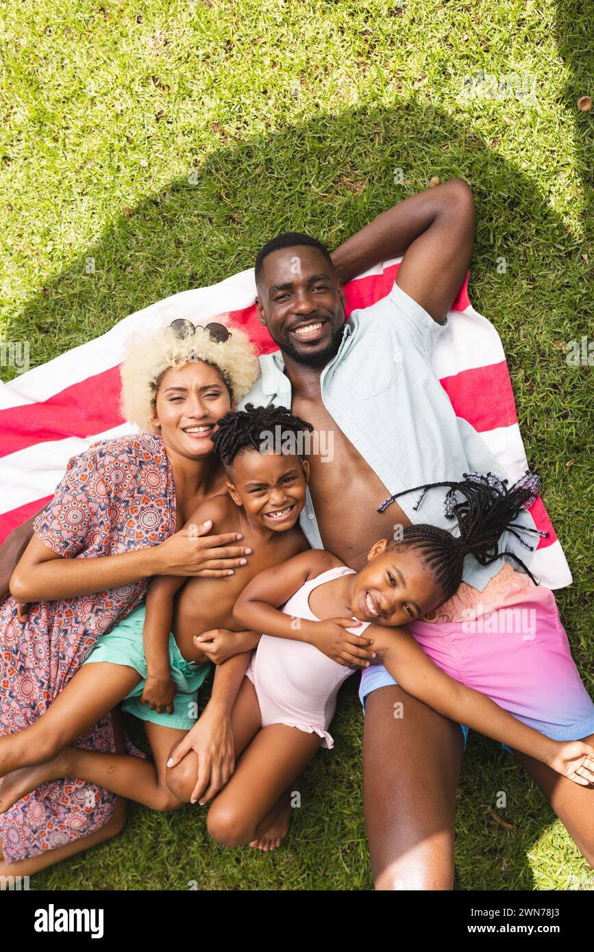 African American man and biracial woman lie on a blanket with a boy and girl, all smiling Stock Photo