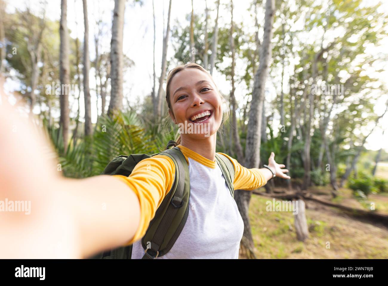 Young Caucasian woman takes a selfie with a beaming smile in a forest setting on a hike Stock Photo