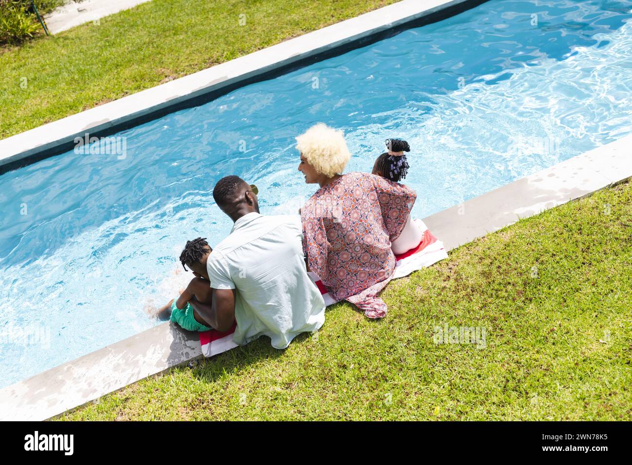 African American family enjoys a sunny day outdoors, with their feet dipped in the water Stock Photo