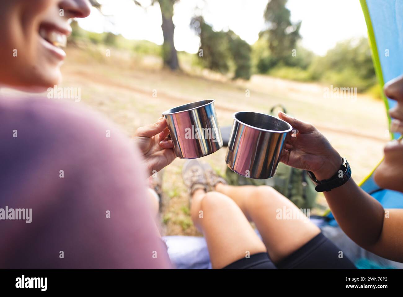 Two women cheer with metal cups, sharing a joyful moment outdoors Stock Photo
