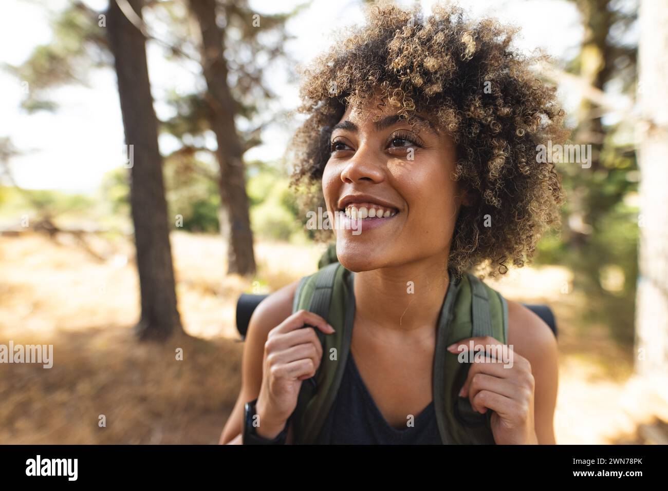 A young biracial woman with curly hair smiles while hiking in a forest ...