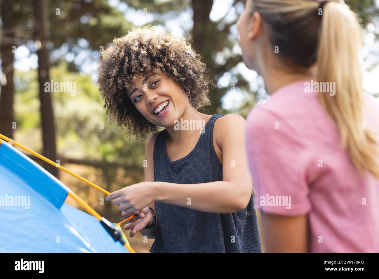 Young biracial woman with curly hair smiles while setting up a blue ...
