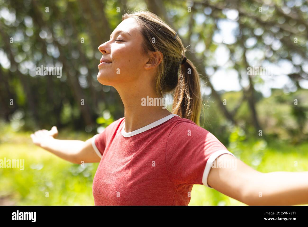 Young woman with her arms outstretched enjoys the sun in a green park Stock Photo