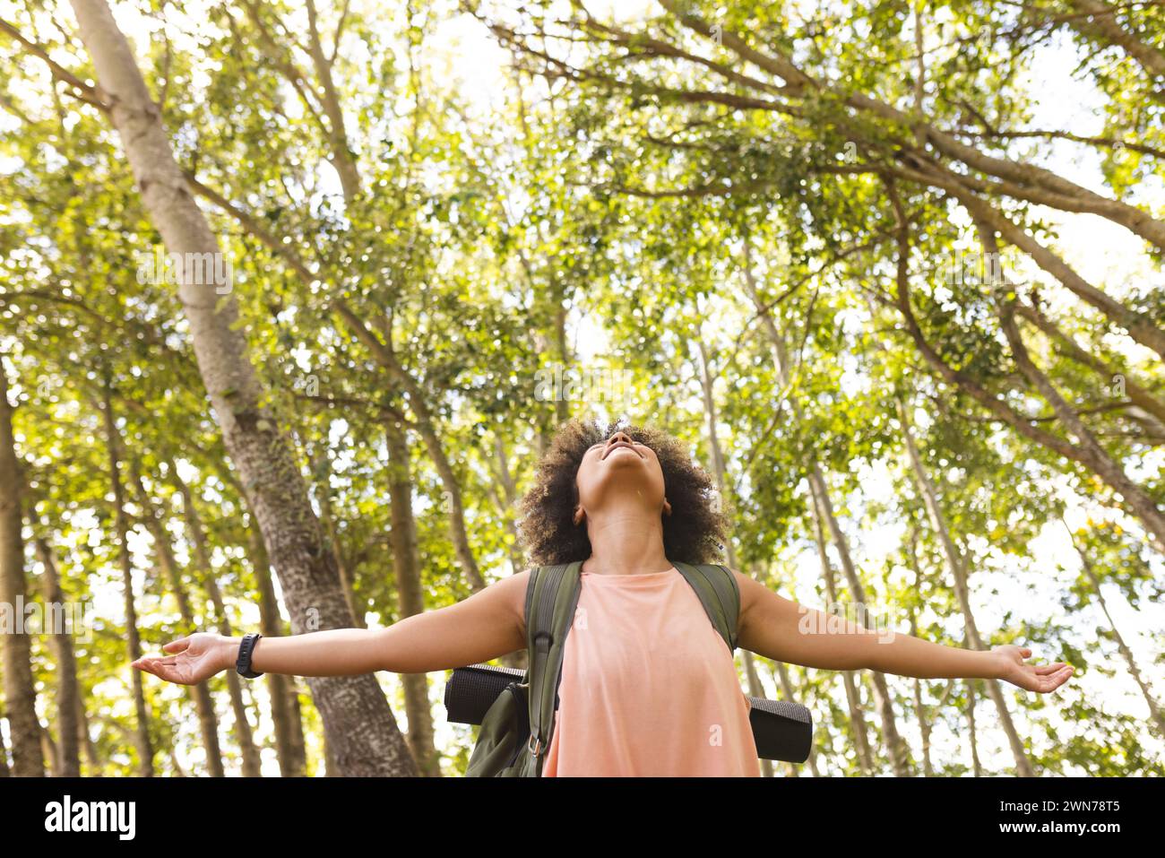 Young biracial woman with arms outstretched, embracing nature in a sunlit forest with copy space Stock Photo