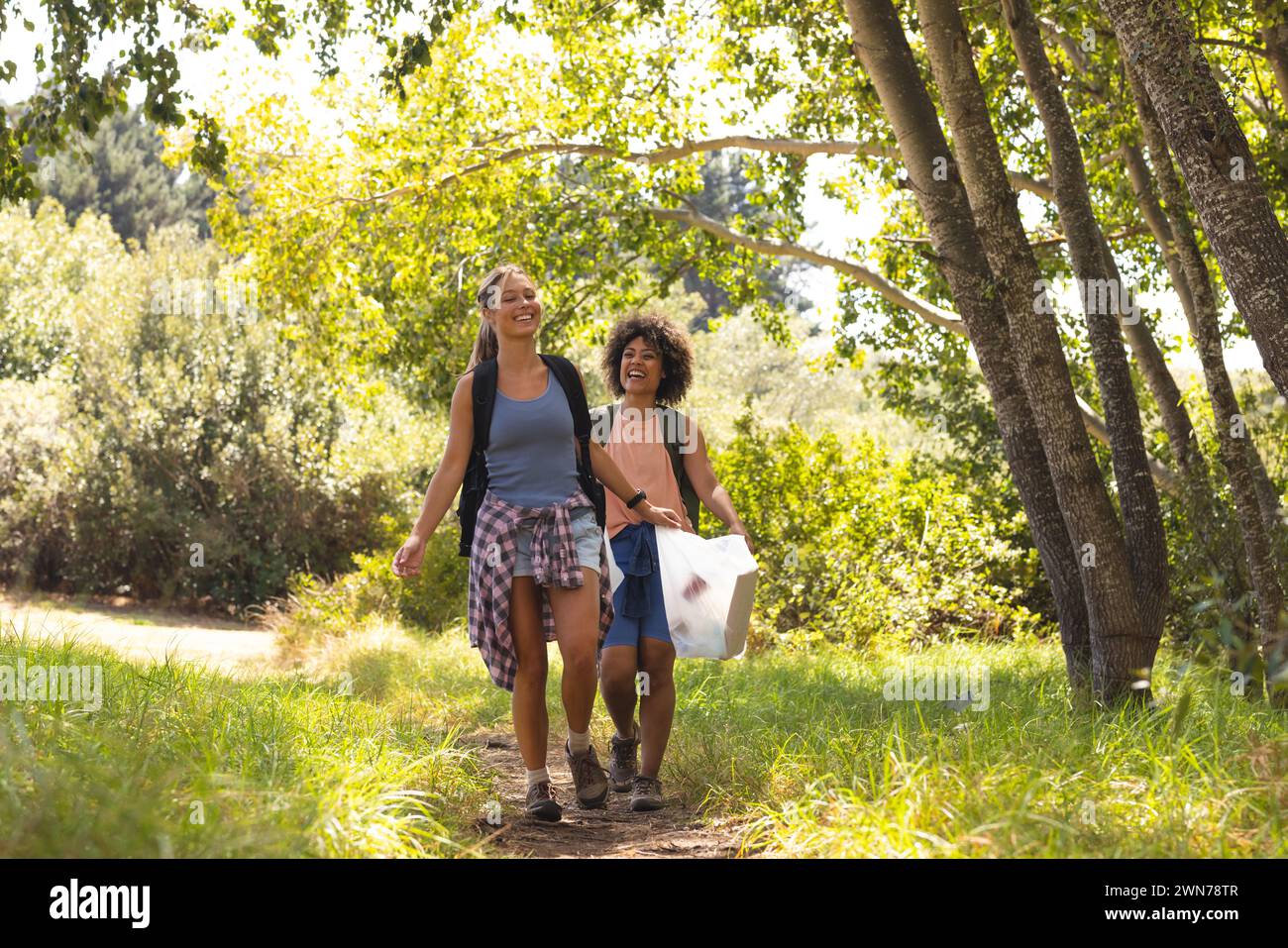 Two women collect trash on a sunny hike, sharing joy. Stock Photo