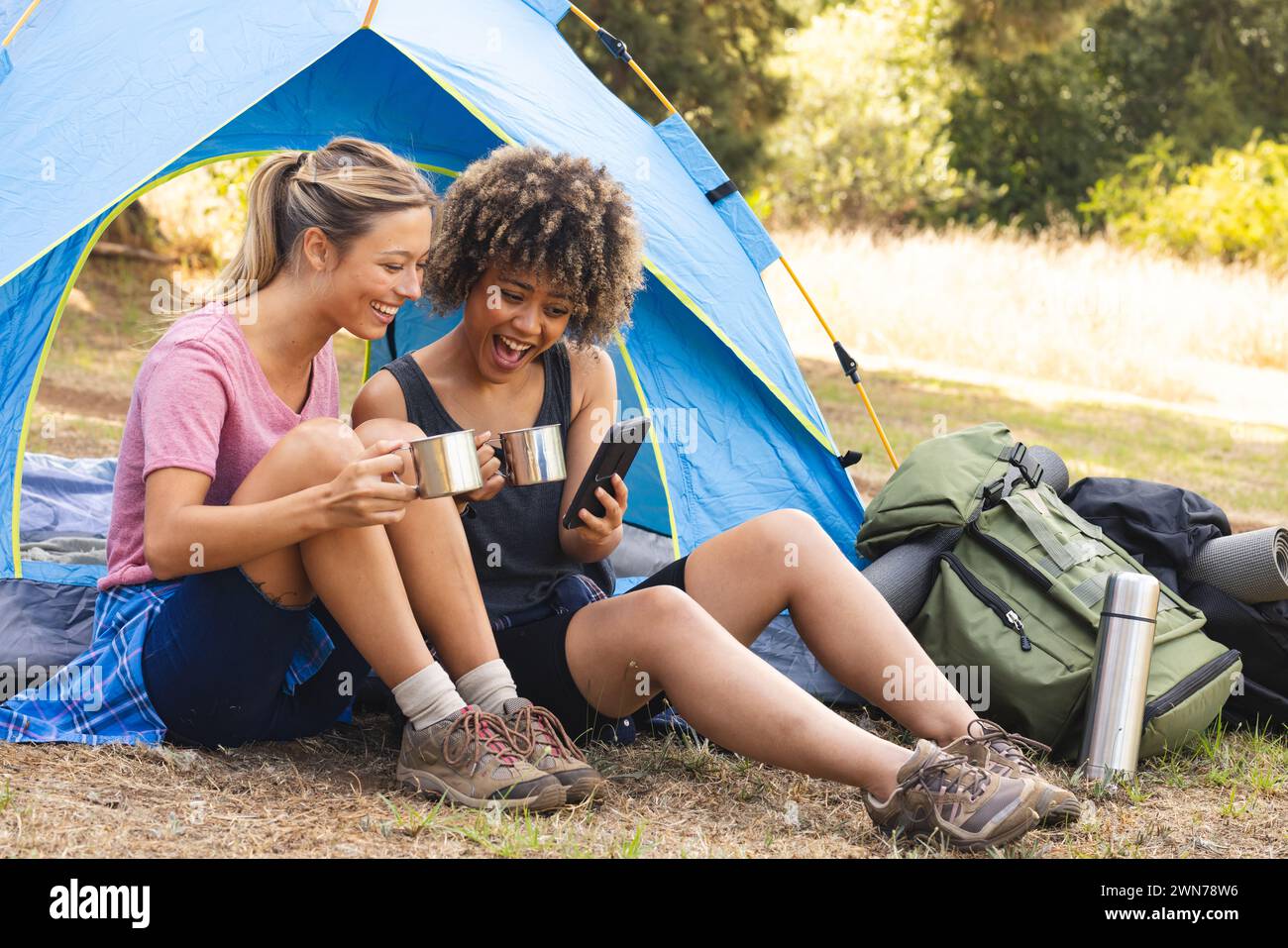 Young Caucasian woman and biracial woman share a laugh outside a tent Stock Photo