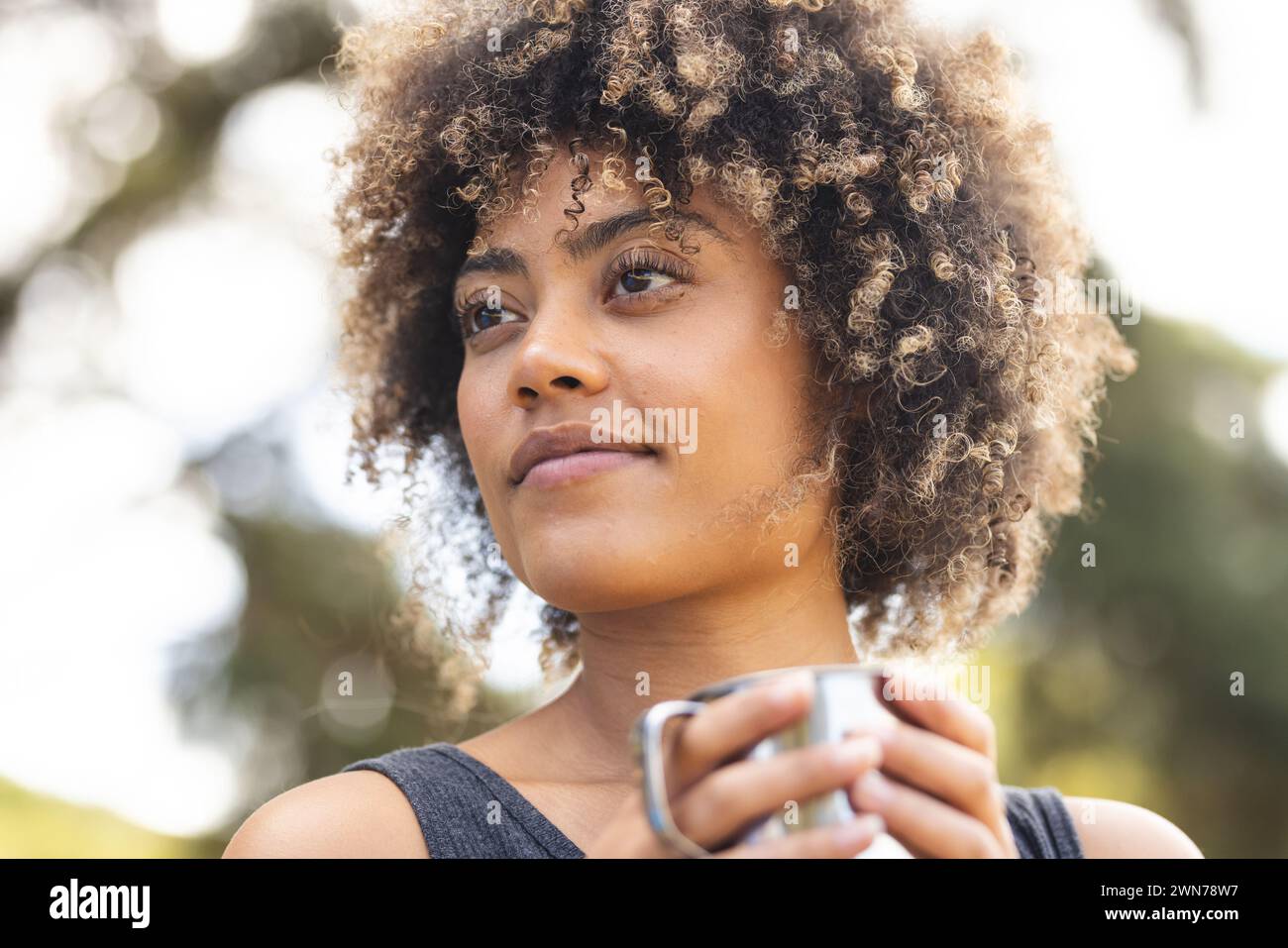 A young biracial woman with curly hair holds a cup outdoors Stock Photo ...