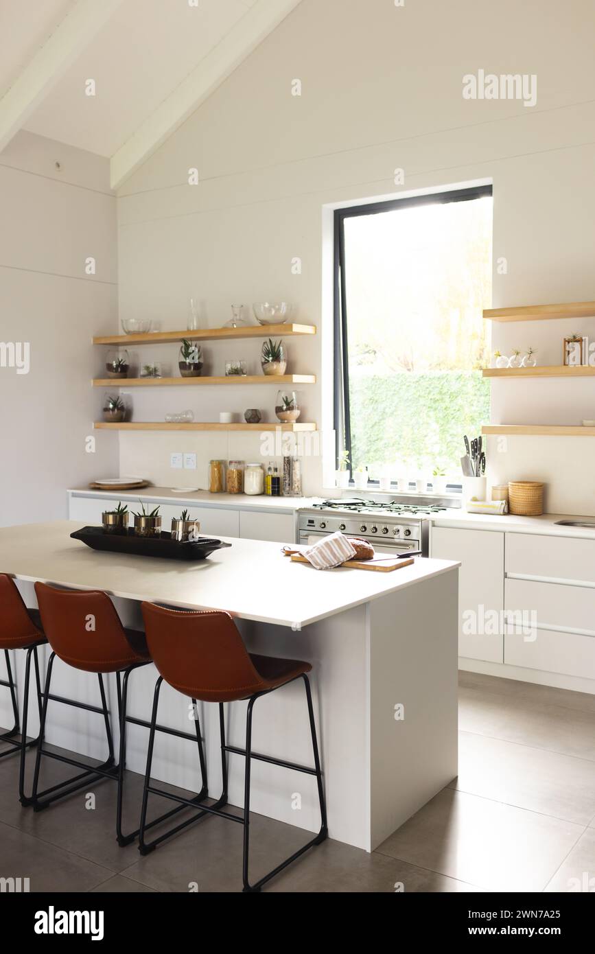 Modern kitchen with white cabinets, island, open shelves, and ample natural light. Stock Photo