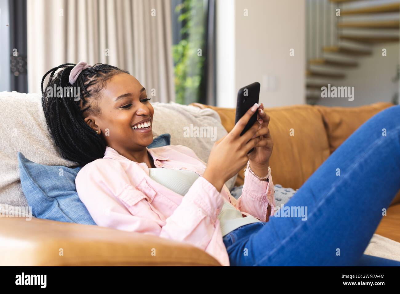 Young African American woman smiles while using her smartphone Stock Photo