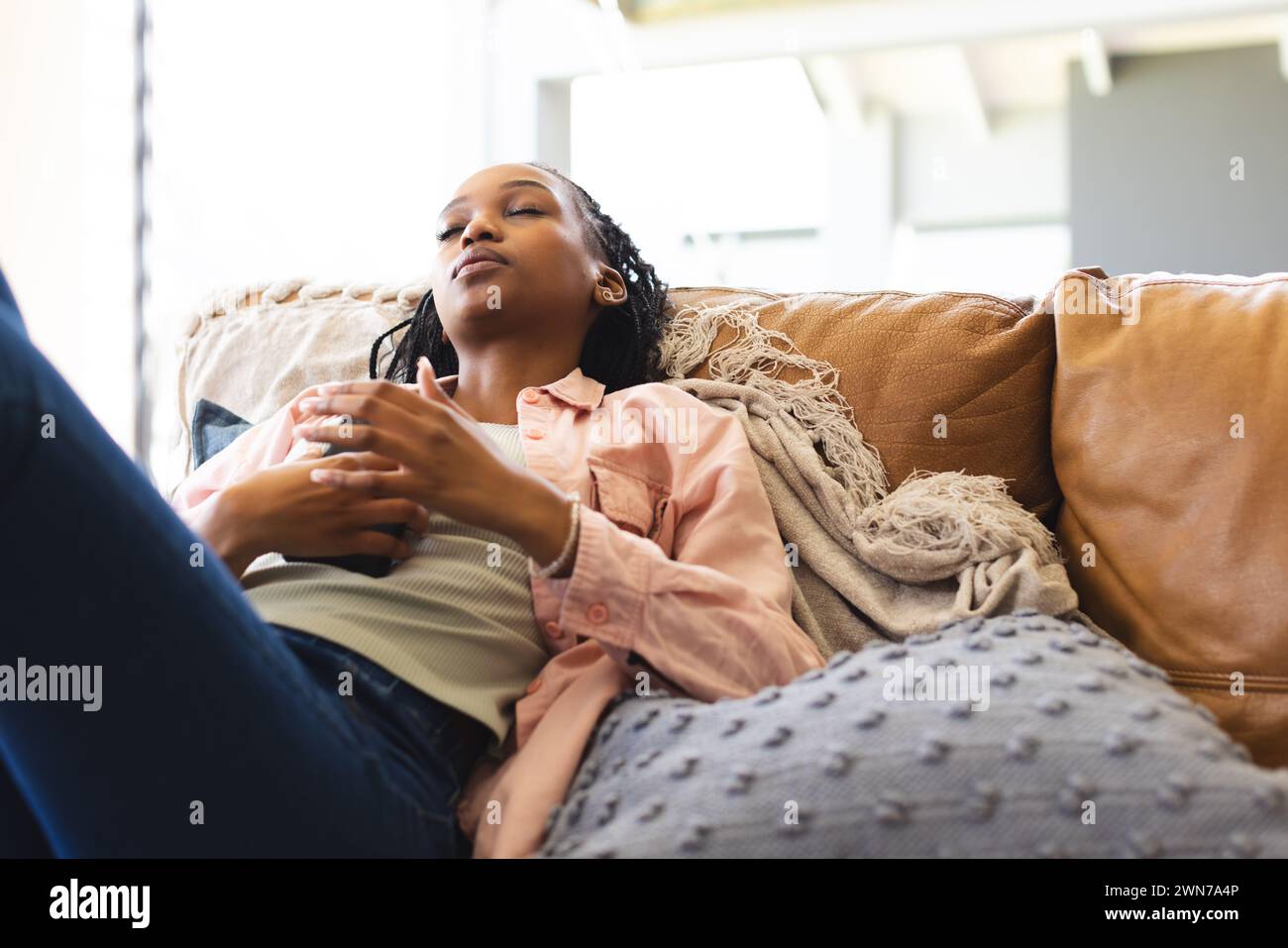 A young African American woman relaxes on a couch, eyes closed and ...