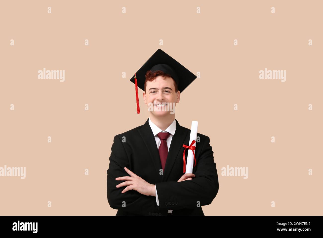 Happy male student in mortar board with diploma on beige background ...