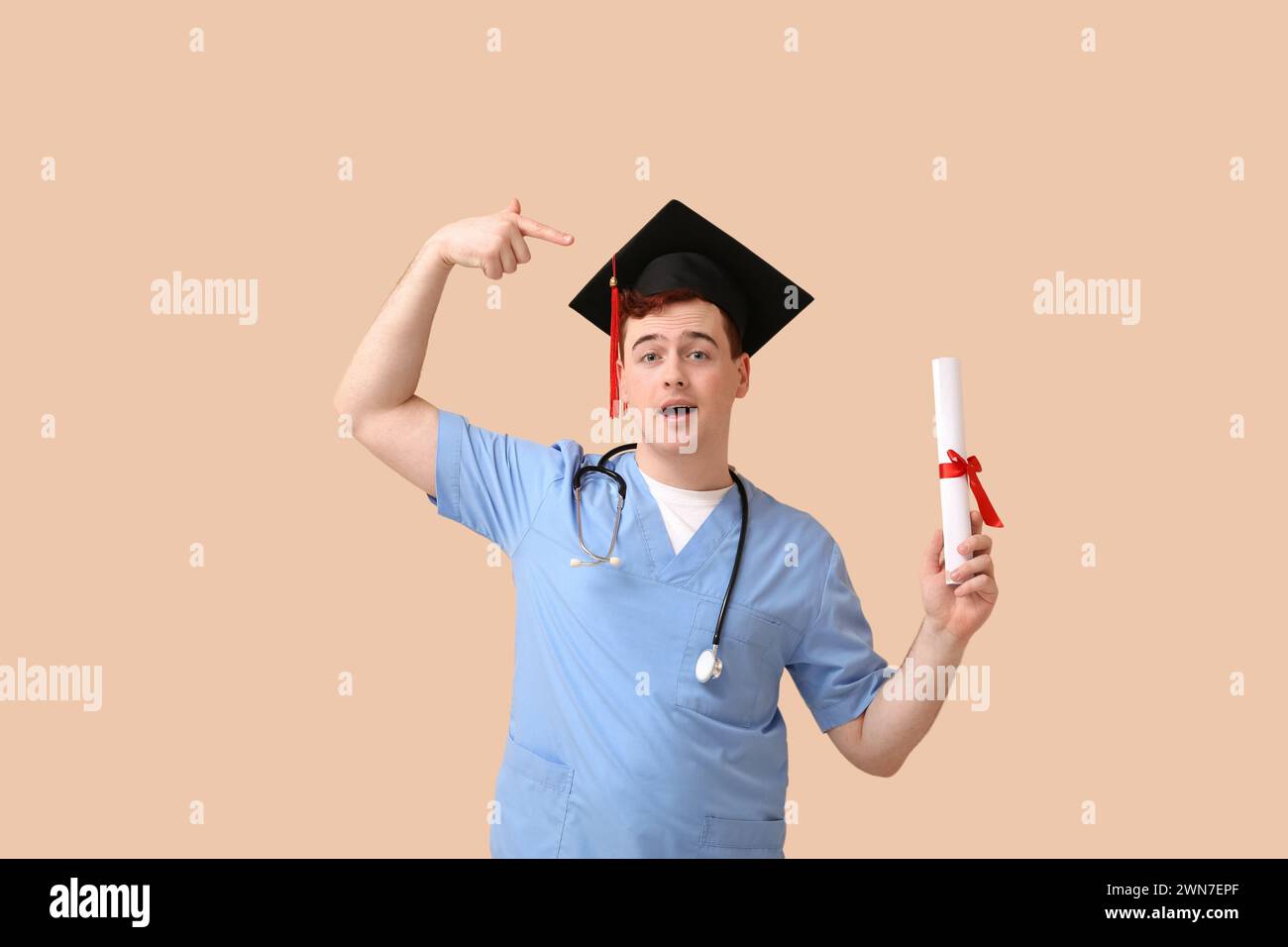 Male student in mortar board and uniform of doctor with diploma showing ...
