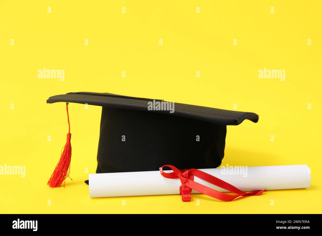 Mortar board and diploma on yellow background Stock Photo - Alamy