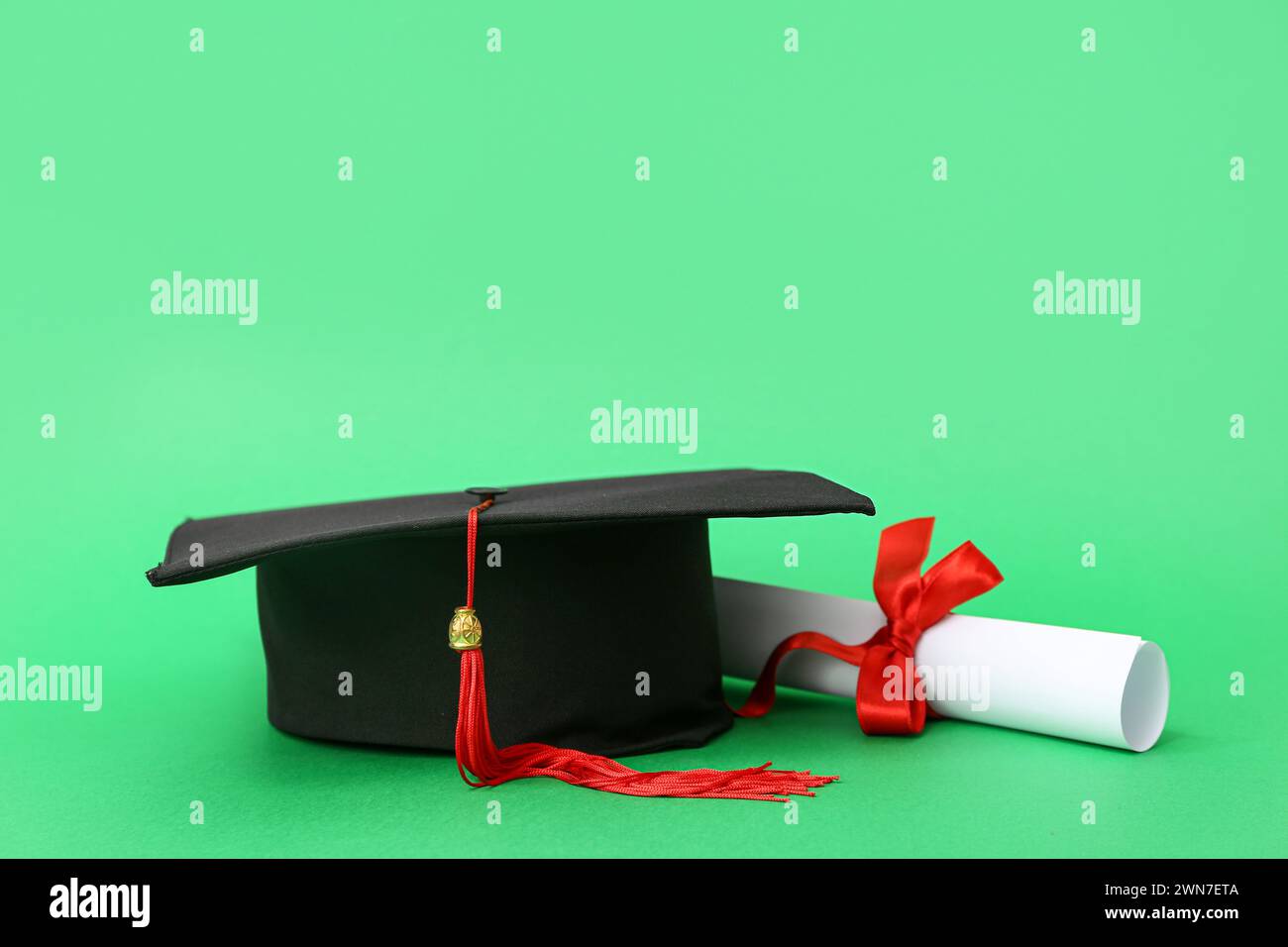 Mortar board and diploma on green background Stock Photo - Alamy