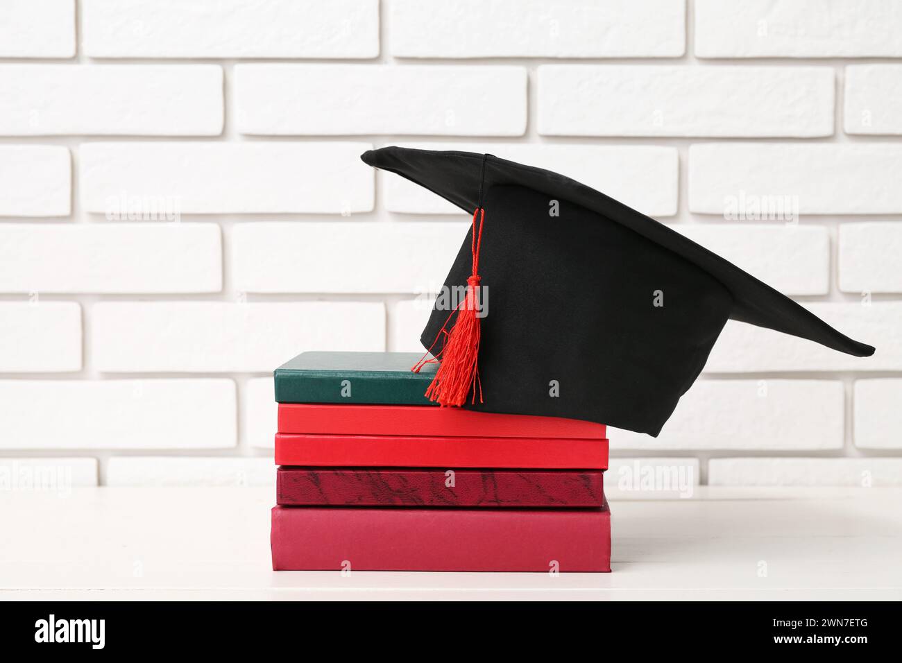 Mortar board and books on table near white brick wall Stock Photo - Alamy