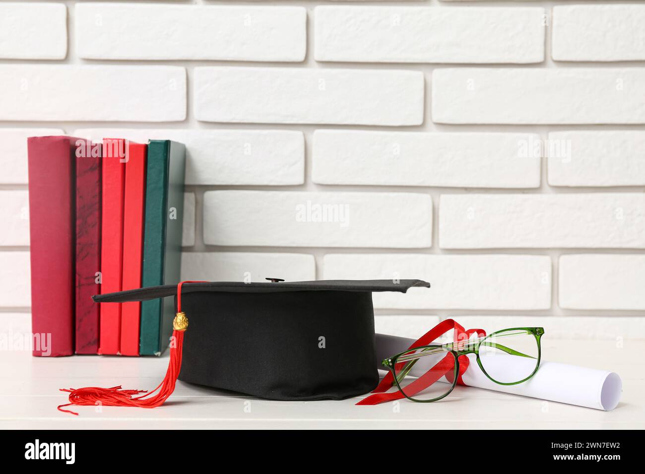 Mortar board with diploma, eyeglasses and books on table near white ...