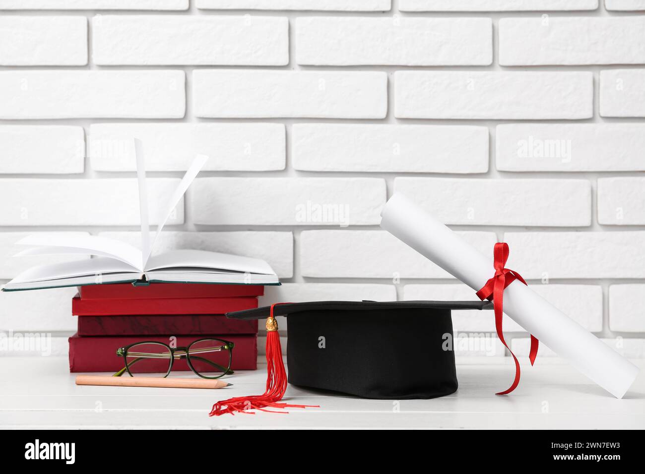 Mortar board with diploma, eyeglasses and books on table near white