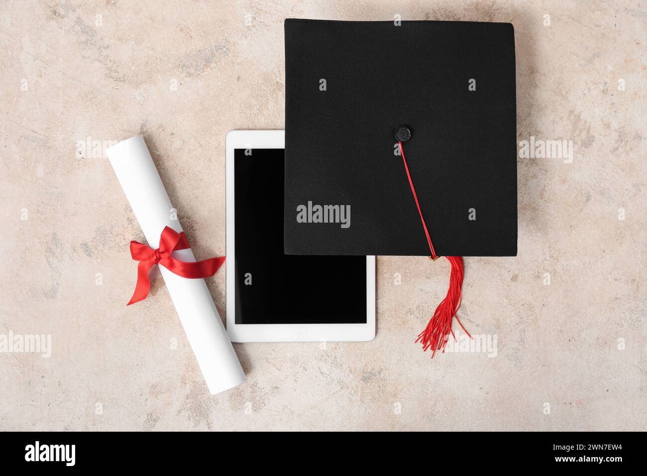 Mortar board with diploma and modern tablet computer on beige ...