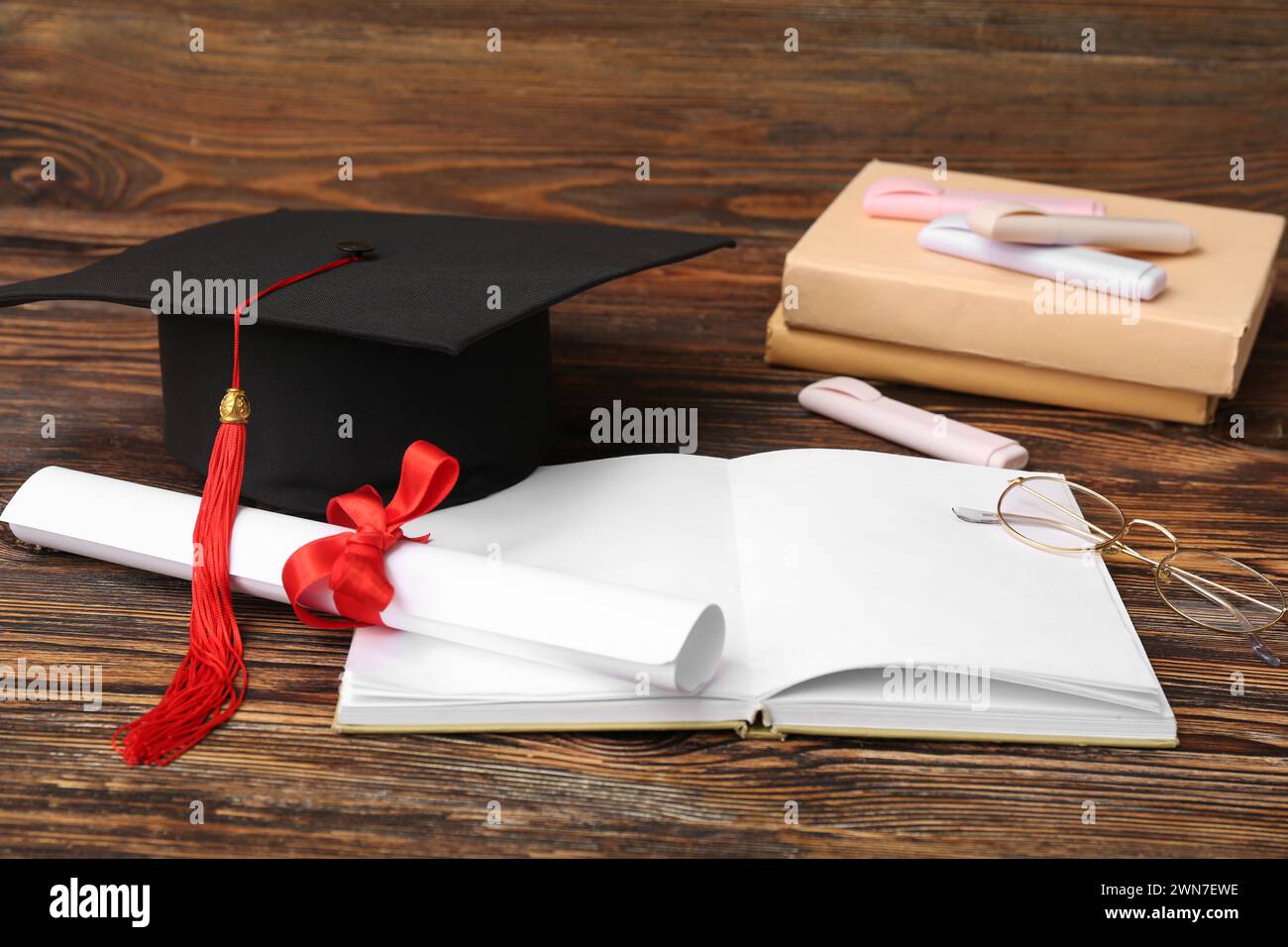 Mortar board with diploma, book and eyeglasses on wooden background ...
