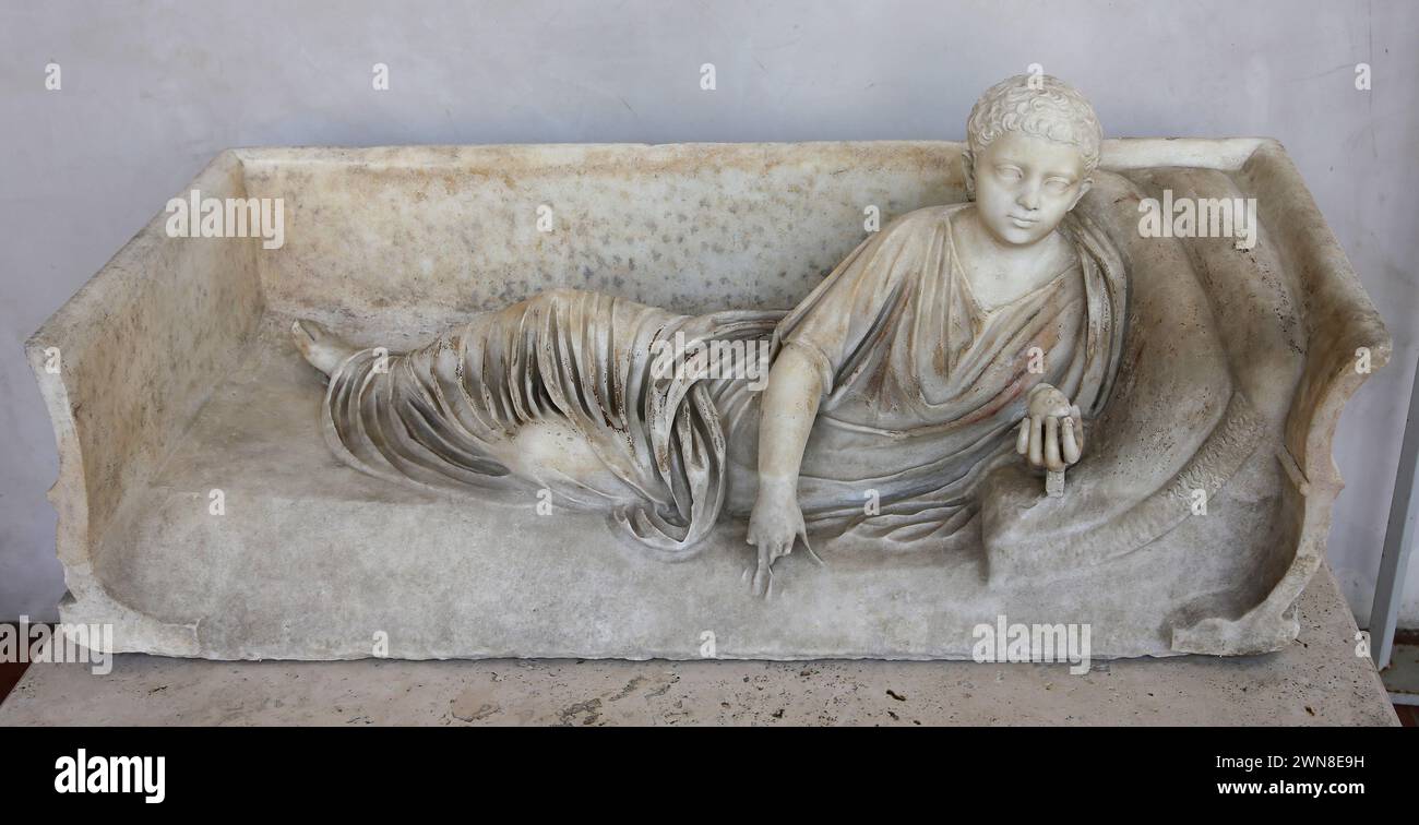 Roman sarcophagus with statue of reclining boy holding a fruit. Rome. National Roman Museum (Baths of Diocletian). Rome. Italy. Stock Photo
