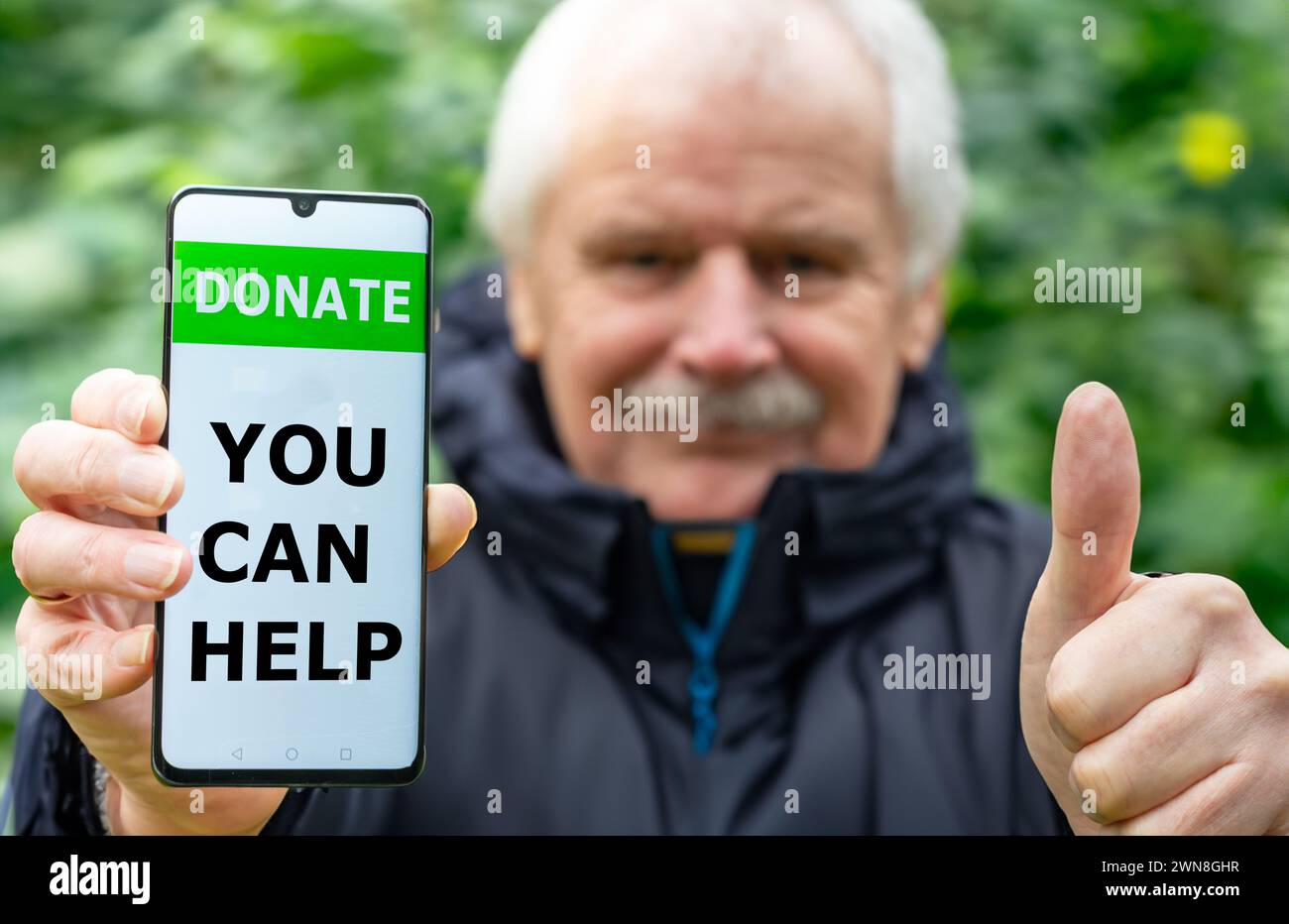 Elder man shows a mobile phone with the test 'donate, you can help'. Stock Photo