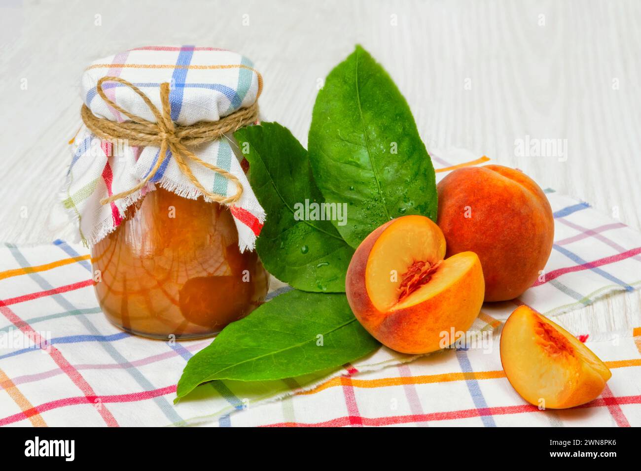 Jam of peaches on the table in a jar, next to a bowl of jam and spoons, peaches Stock Photo