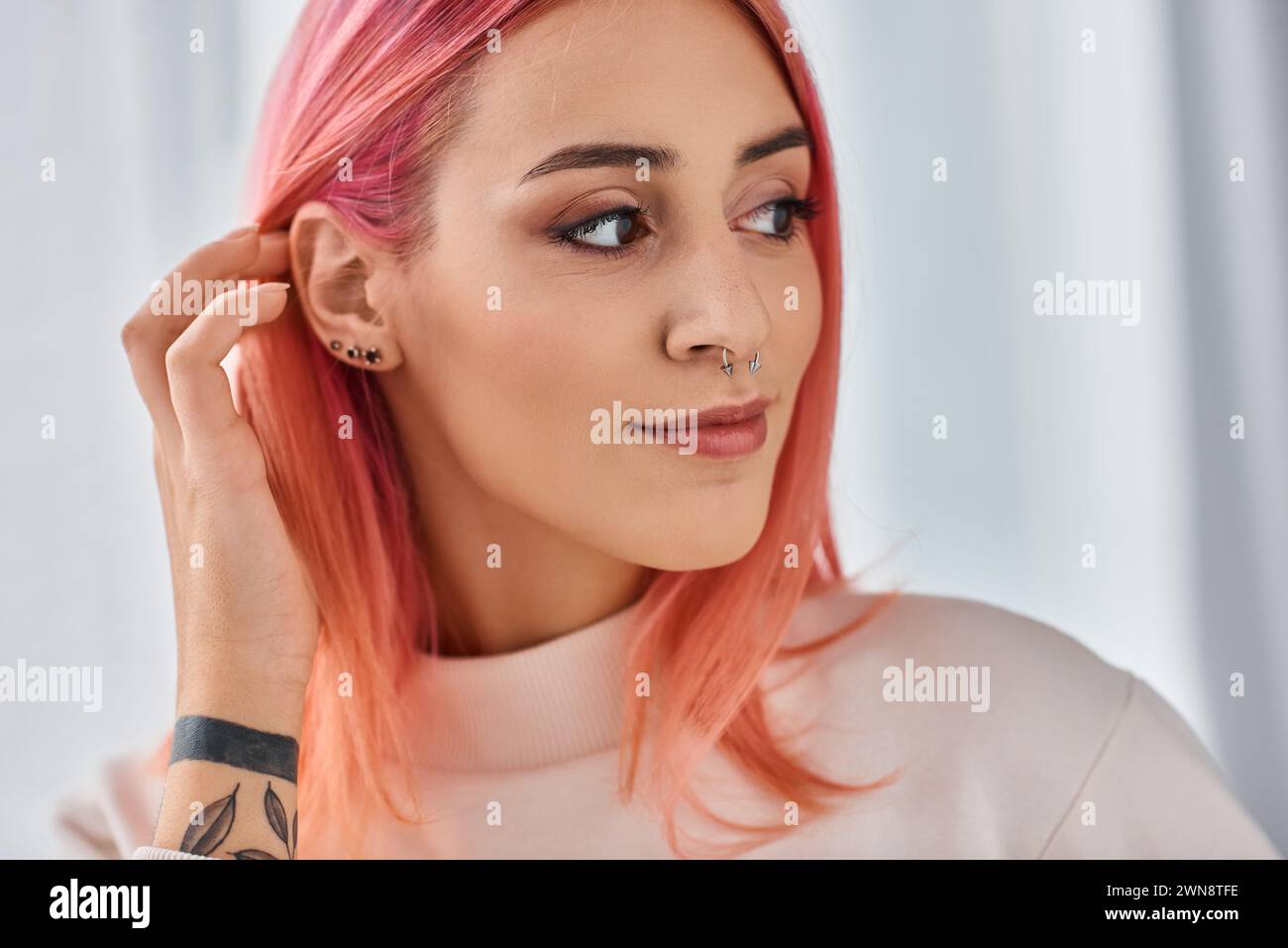 appealing young  jolly woman with pink hair in white jumper posing in kitchen and looking away Stock Photo