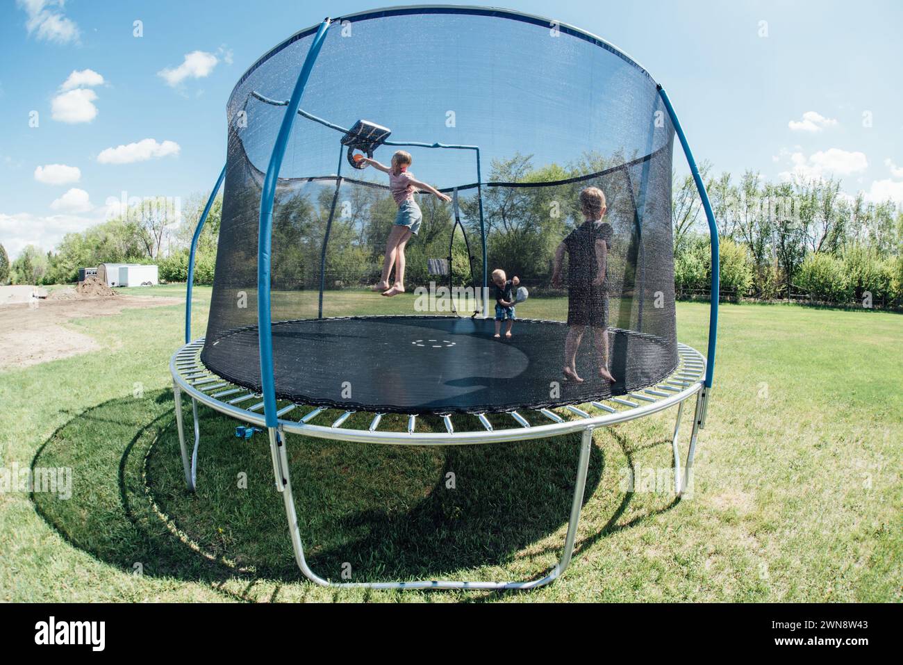 Wide shot of three children playing basketball on trampoline. Stock Photo