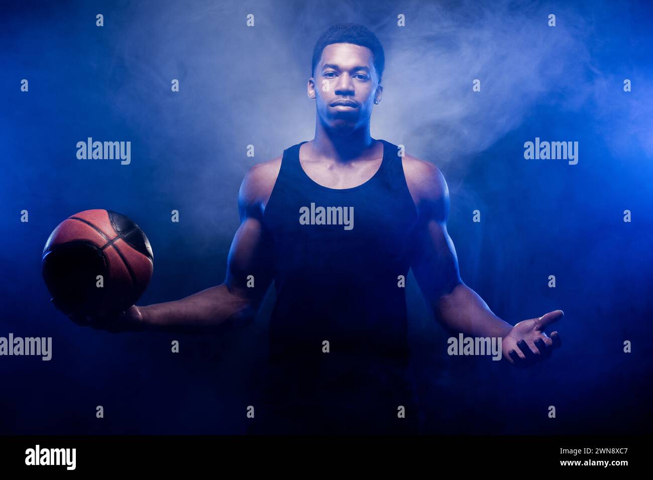 Basketball player lit with blue color posing with a ball against smoke background. Serious concentrated african american man. Stock Photo