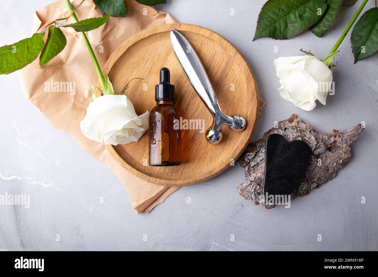Self care composition with facial serum, gua sha, facial roller. Holistic beauty arrangement with roses. Stock Photo