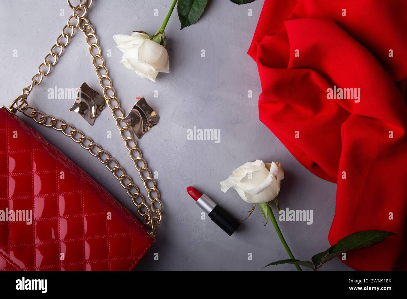 Chic fashion accessories with red purse and classic beauty products among roses. Stock Photo