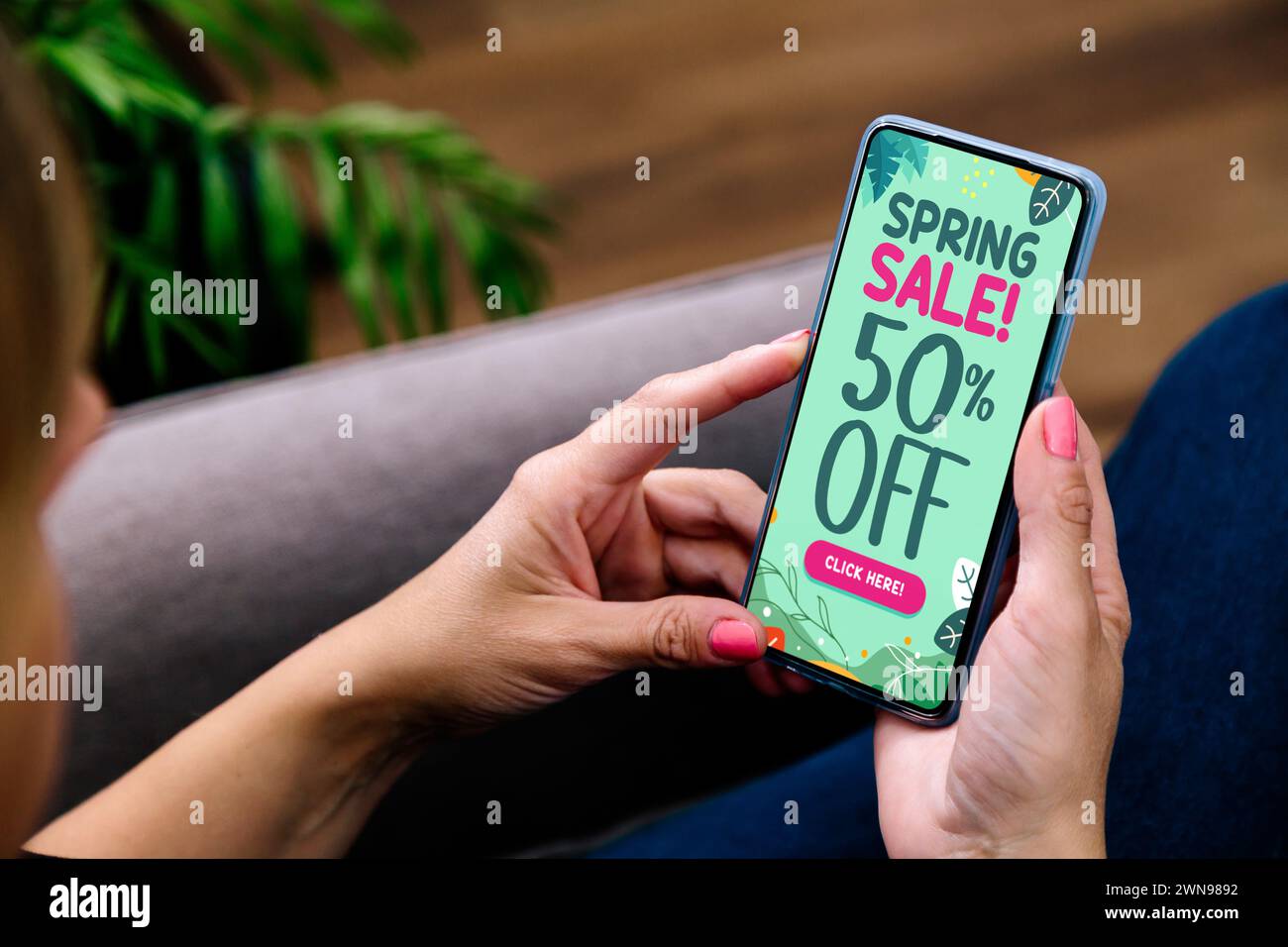 Spring sales offer Ad. Up to 50% off. Woman holding a mobile phone showing an offer or coupon on the screen. Stock Photo