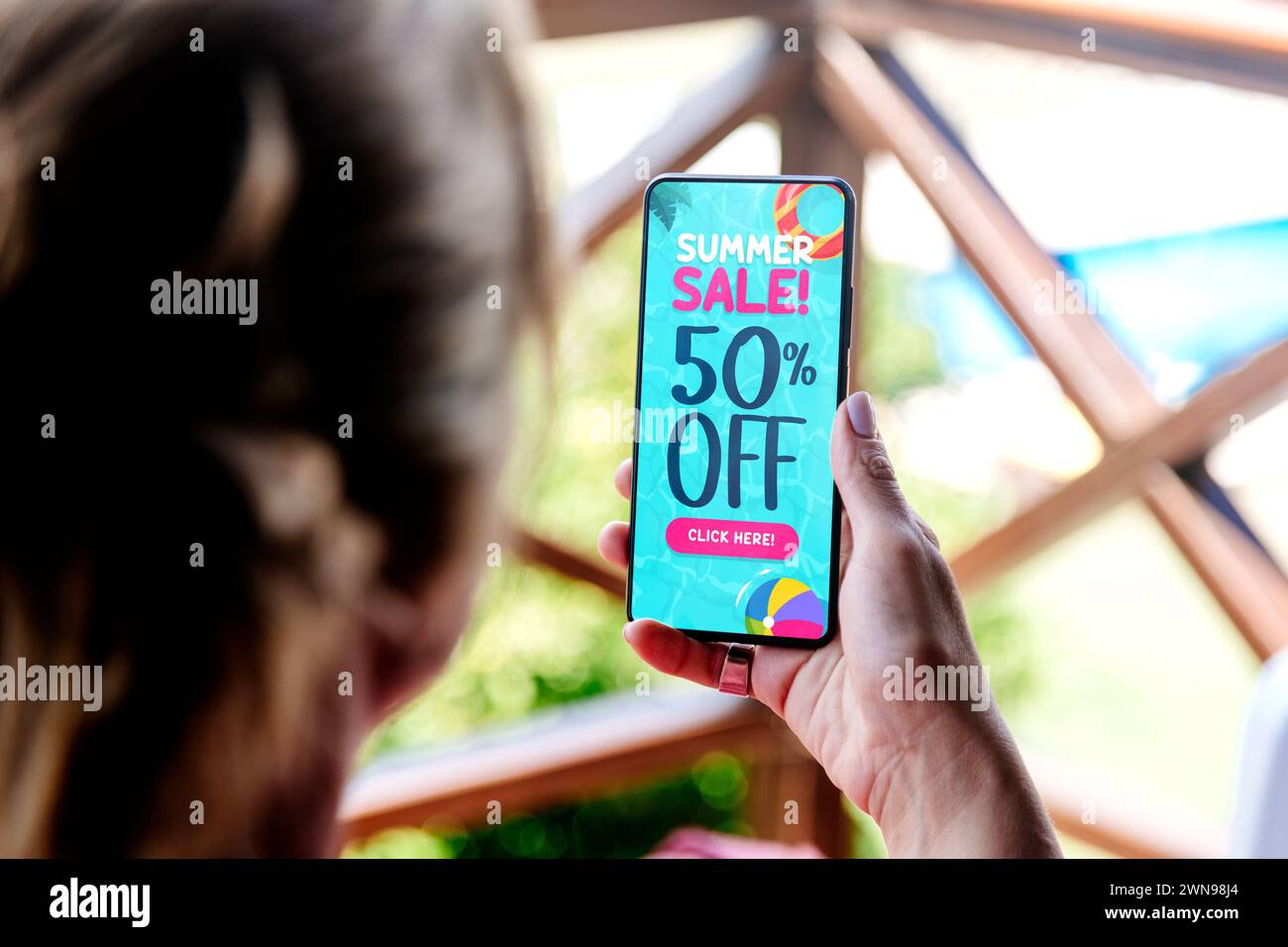 50% off summer sale. Woman holding a mobile phone showing an offer or coupon on the screen. Stock Photo