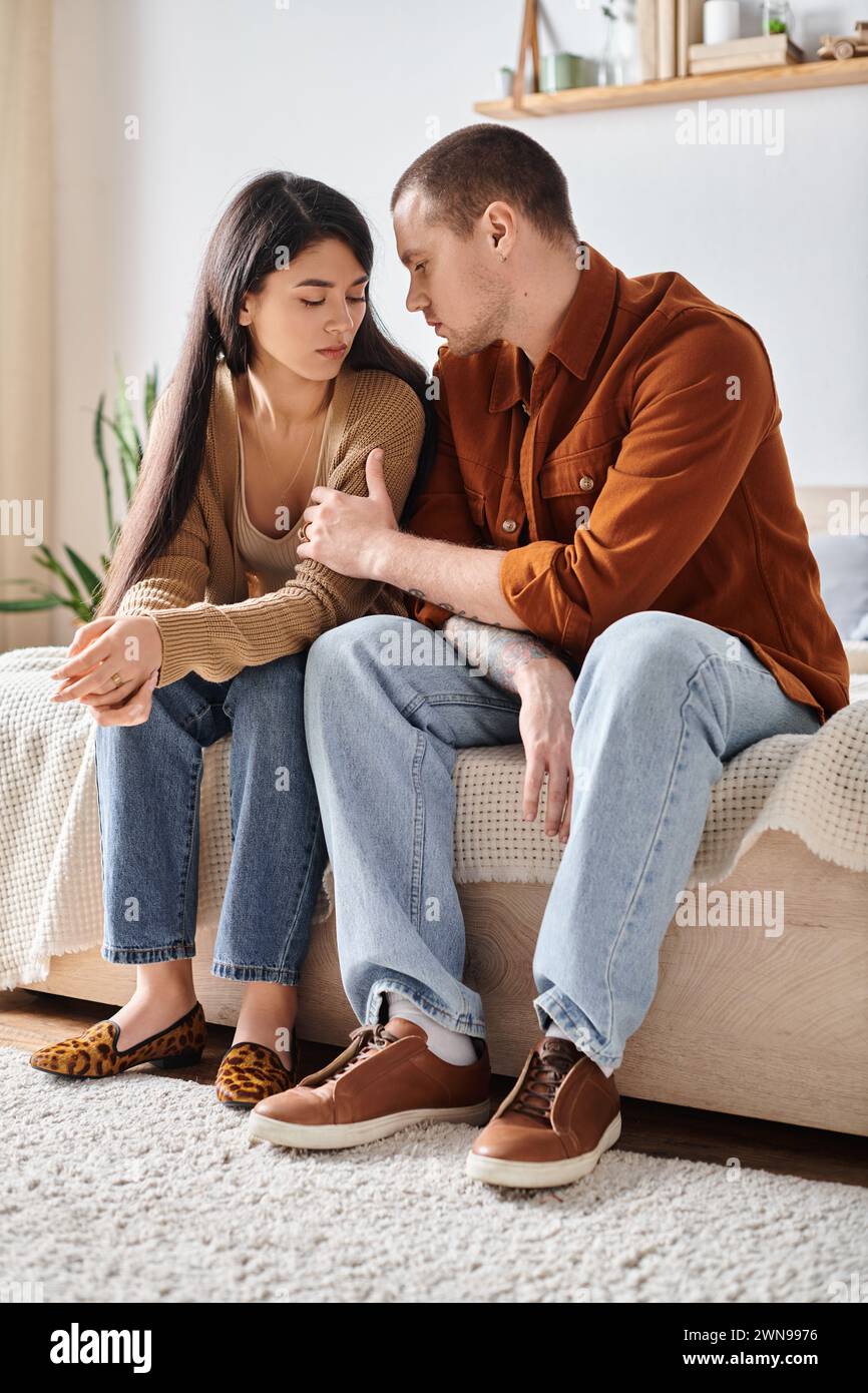 young and tattooed man talking to upset asian wife in bedroom at home, family trouble concept Stock Photo
