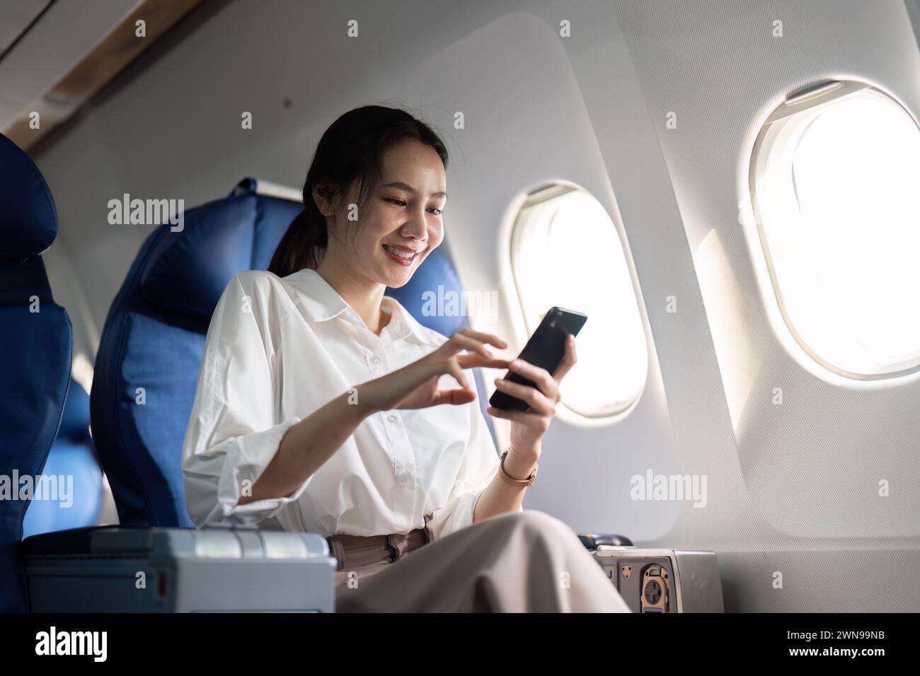 Traveling and technology. Flying at first class. Young business woman passenger using smartphone while sitting in airplane flight Stock Photo