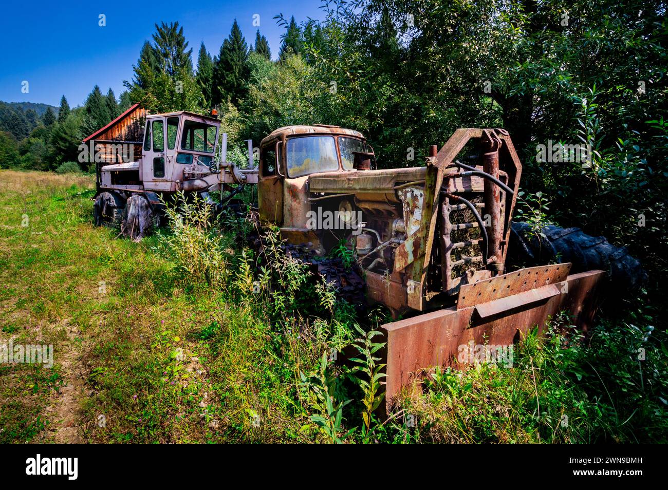 Old, wrecked machinery, abandoned snow blower and machine in the bushes. Rusty, unused, heavy vehicles in a mountain forest. Bieszczady, sunny, summer Stock Photo