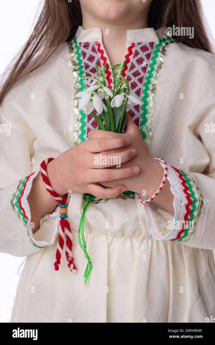 Bulgarian girl in ethnic costume with bouquet of snowdrops and a red and white symbol of the holiday of the spring martenitsa Baba Marta day, Bulgaria Stock Photo