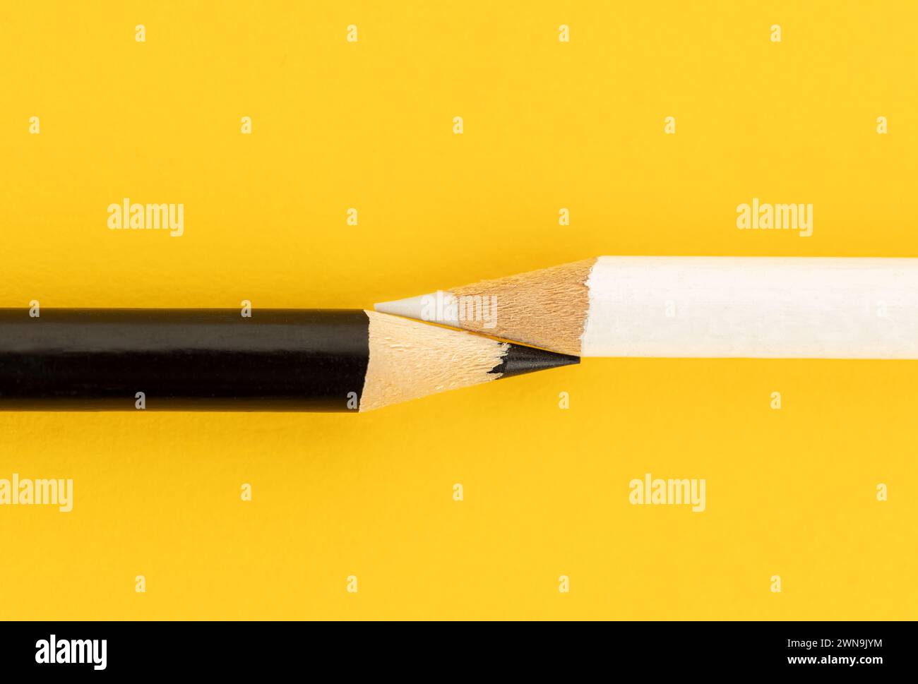 Black pencil and white pencil touching together on yellow background