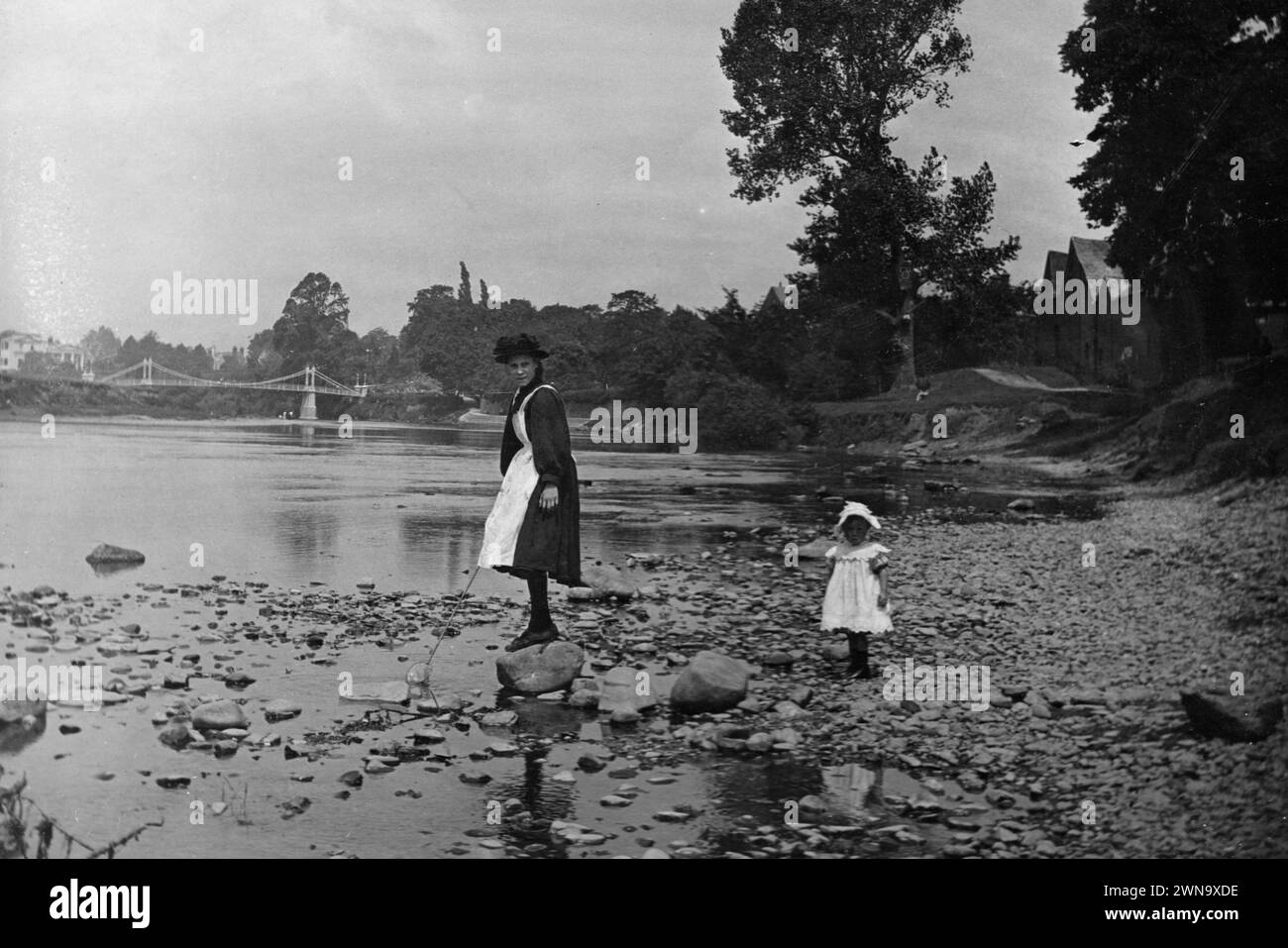 1897 Historic Black and White Photograph of a Nanny and Child by the River Wye with Victoria Bridge, Hereford, Herefordshire, England, UK Stock Photo