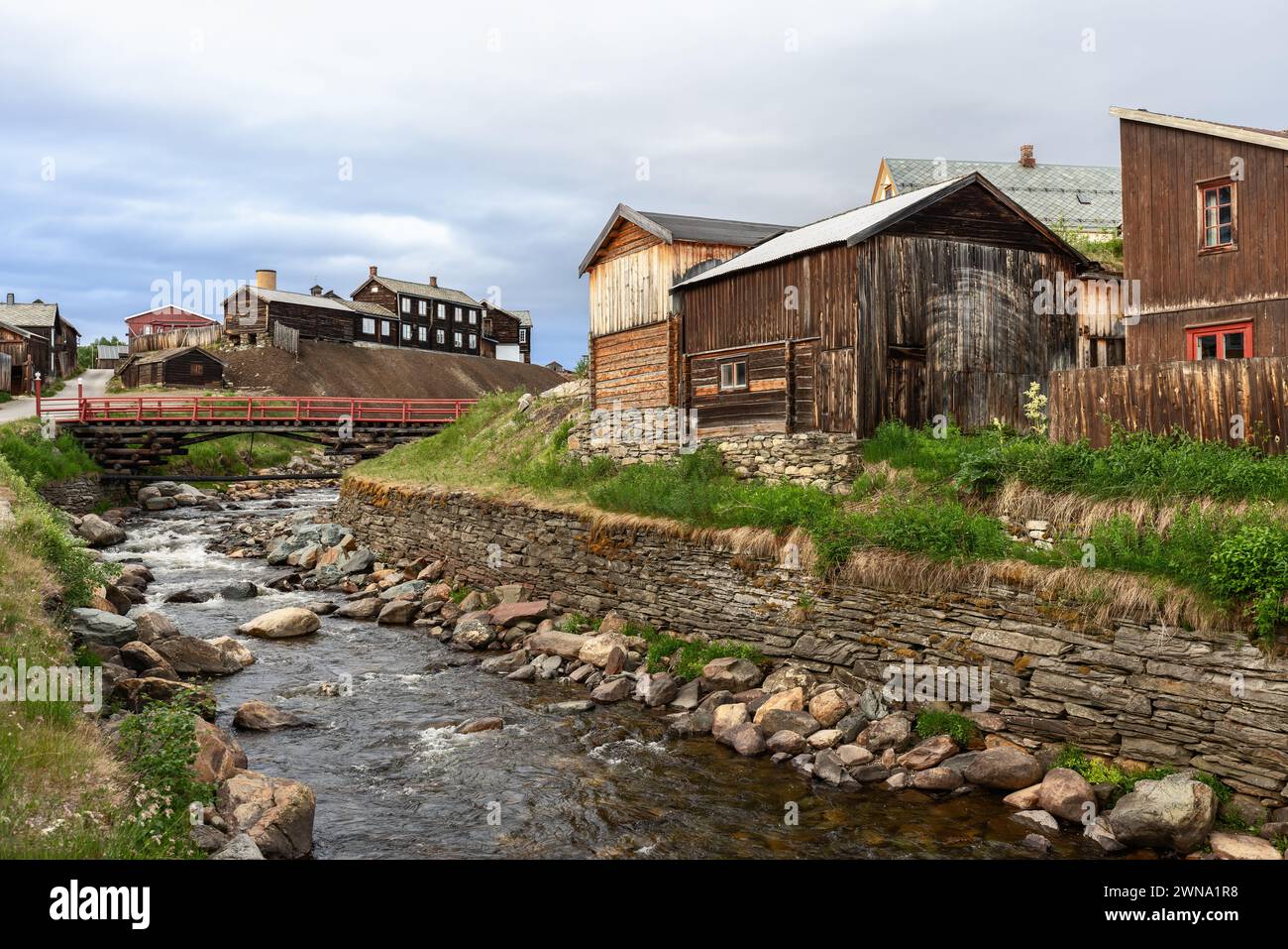 In Roros, a vibrant red bridge crosses the bustling Glomma River, surrounded by historic wooden buildings Stock Photo