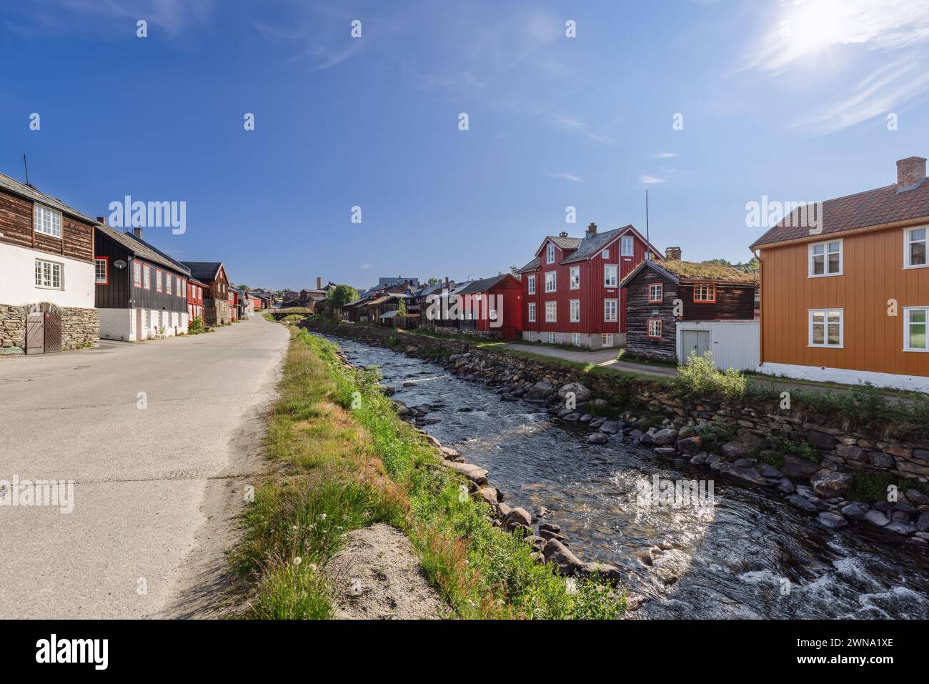 A road runs parallel to the Glomma River in Roros, flanked by a charming row of traditional wooden houses basking in the Nordic sunlight Stock Photo