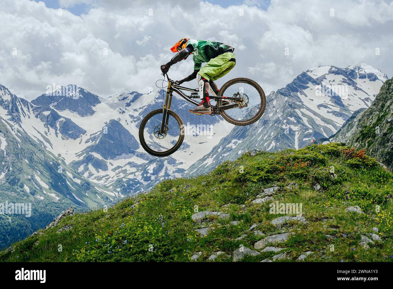 Mountain biker jumped, soaring mid-air against backdrop of snow-capped peaks and lush greenery. downhill competition Stock Photo