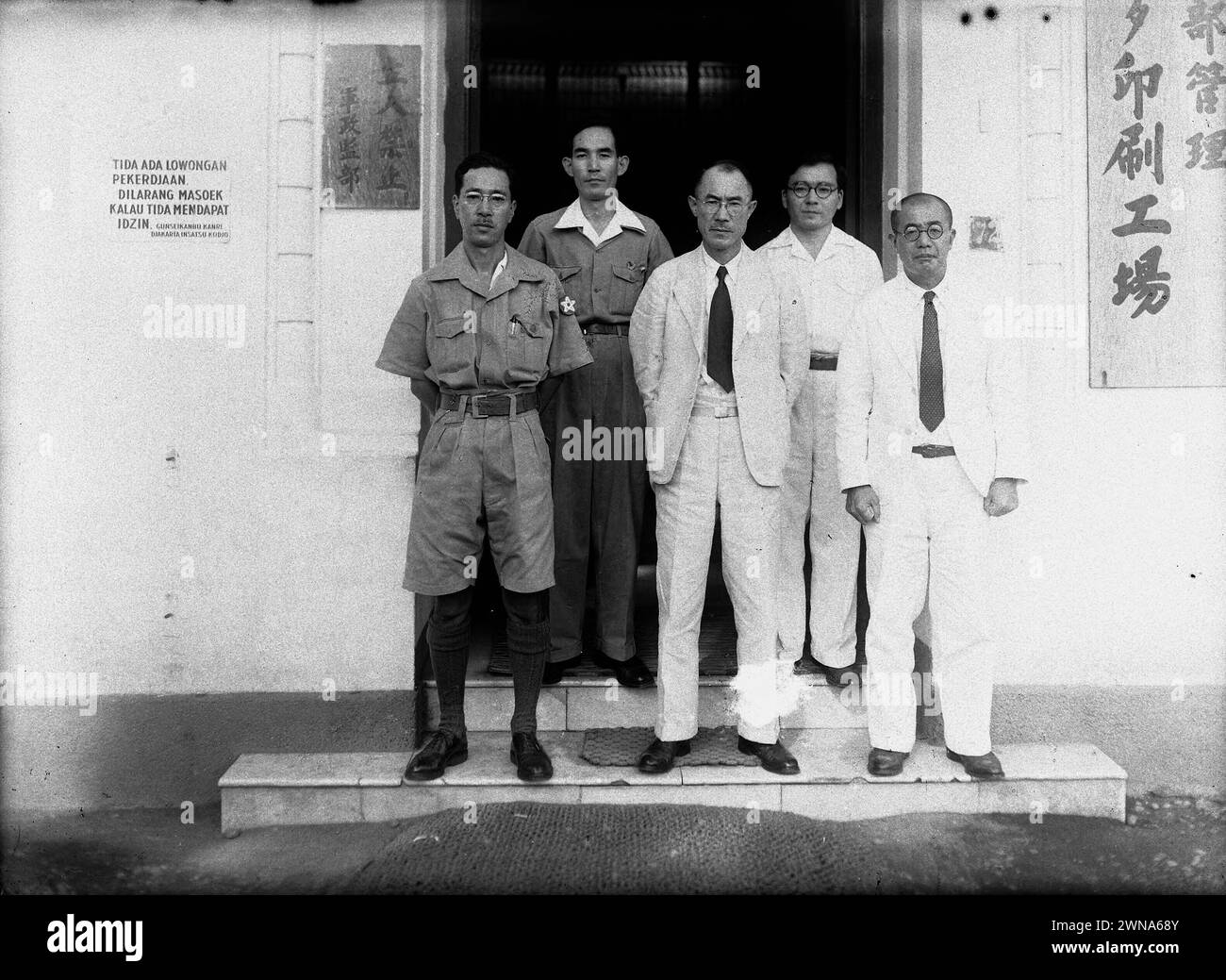 Two Japanese Officers and Three Japanese Civilians in front of an office building in Indonesia (Tidak Ada Lowongan Pekerdjaan) 1942-1945 Stock Photo