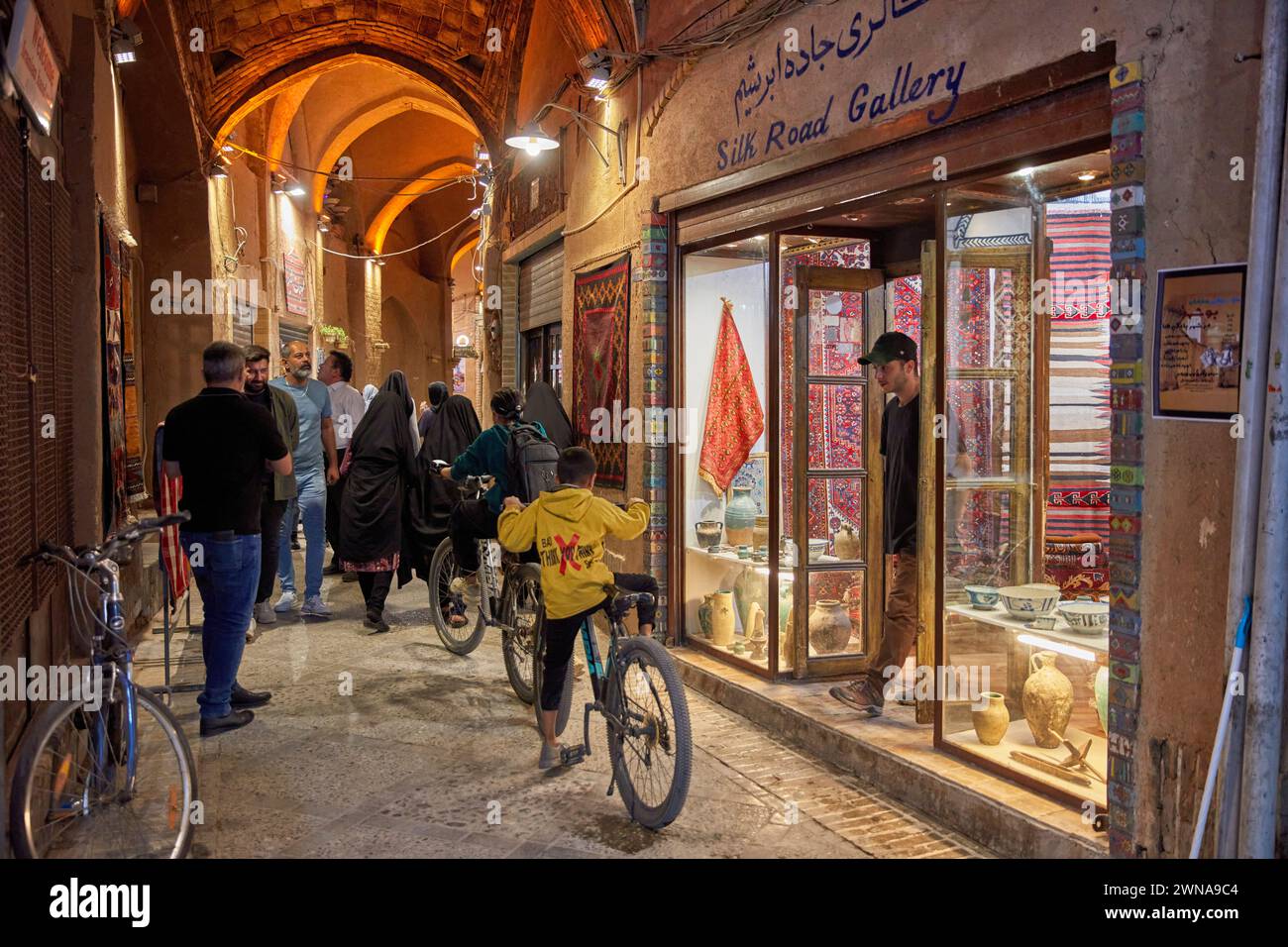 Local people walk in a narrow covered street brightly illuminated at night. Old City of Yazd, Iran. Stock Photo