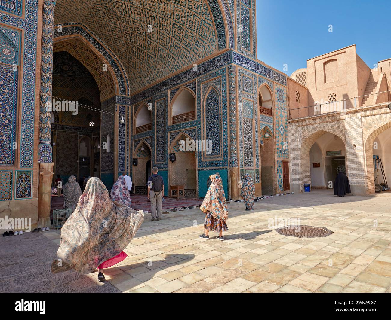 Woman with her chador flowing in the wind walks to the entrance of the Jameh Mosque of Yazd, 14th-century Shia mosque in the Old Town of Yazd, Iran. Stock Photo