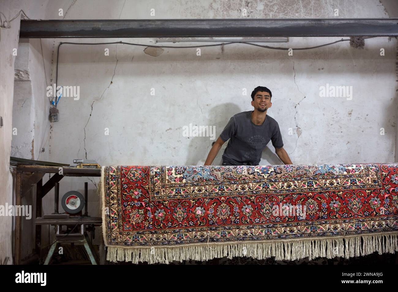 A worker rolls finished carpet in a small carpet making workshop. Yazd, Iran. Stock Photo