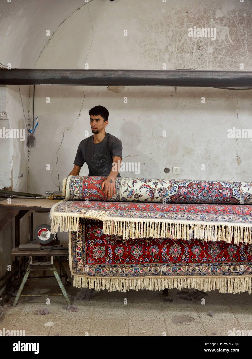 A worker rolls finished carpet in a small carpet making workshop. Yazd, Iran. Stock Photo