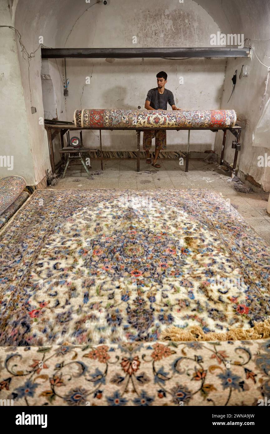 A worker rolls finished carpet in a small carpet making workshop. Yazd, Iran. Stock Photo